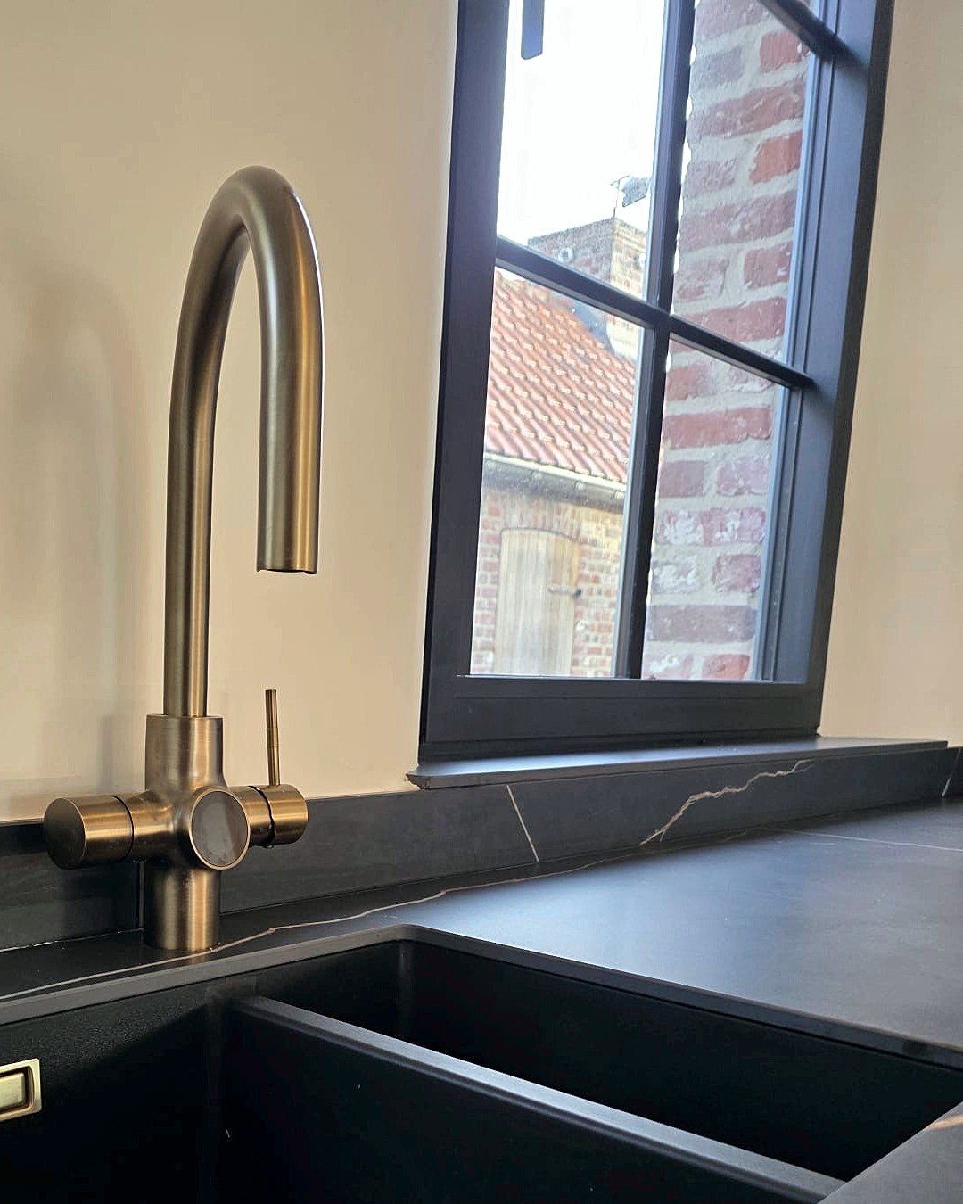 Een kraan in messingkleur boven een zwarte dubbele spoelbak