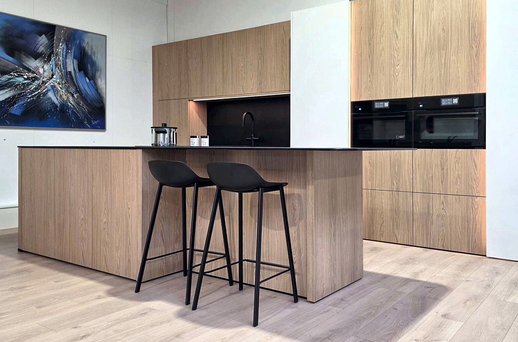 Dezelfde keuken van opzij: het eiland in eik en de kastenwand met een verlichte nis