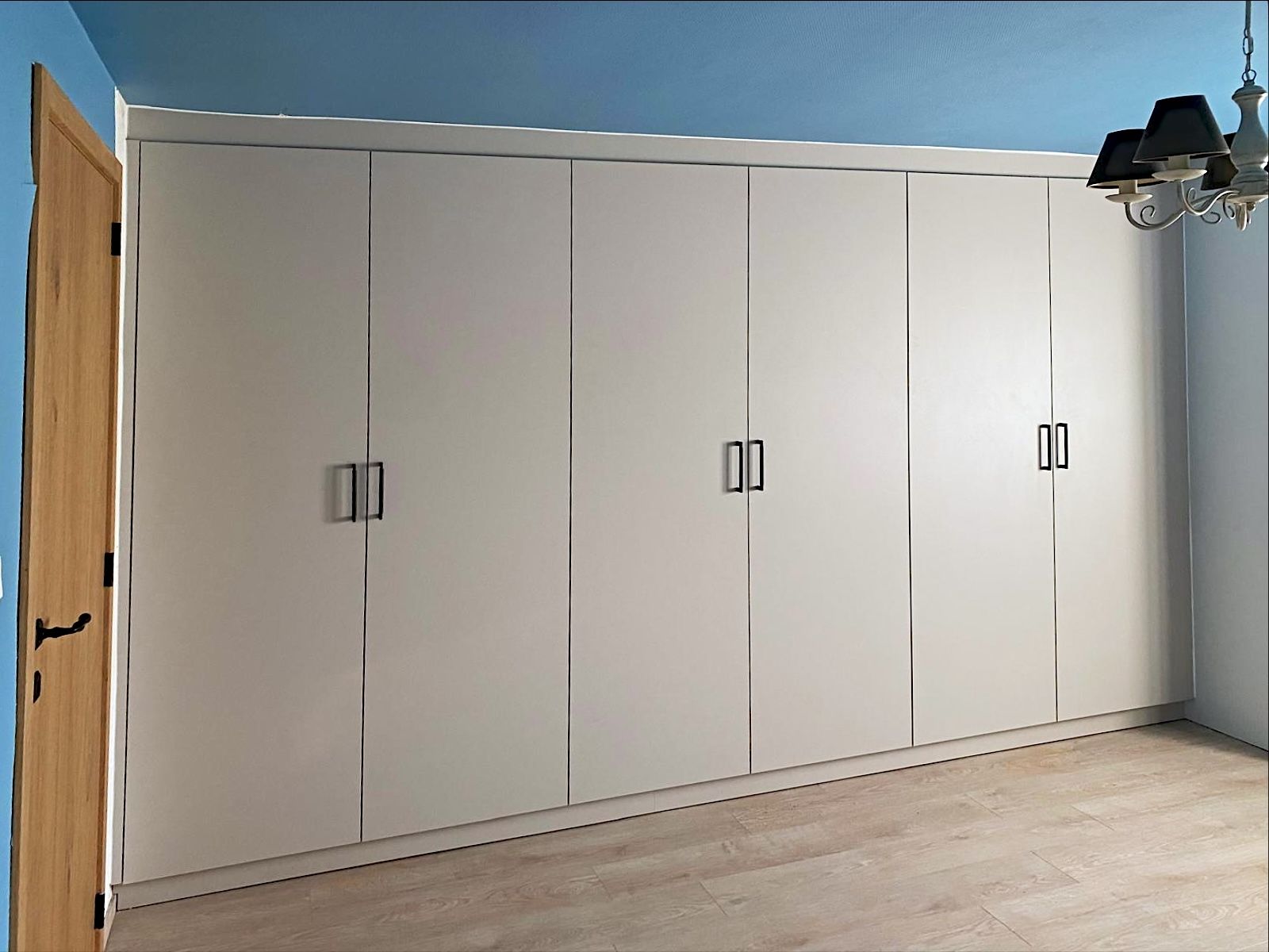 Witte kastenwand met zes deuren en zwarte grepen in een slaapkamer met blauwe muren