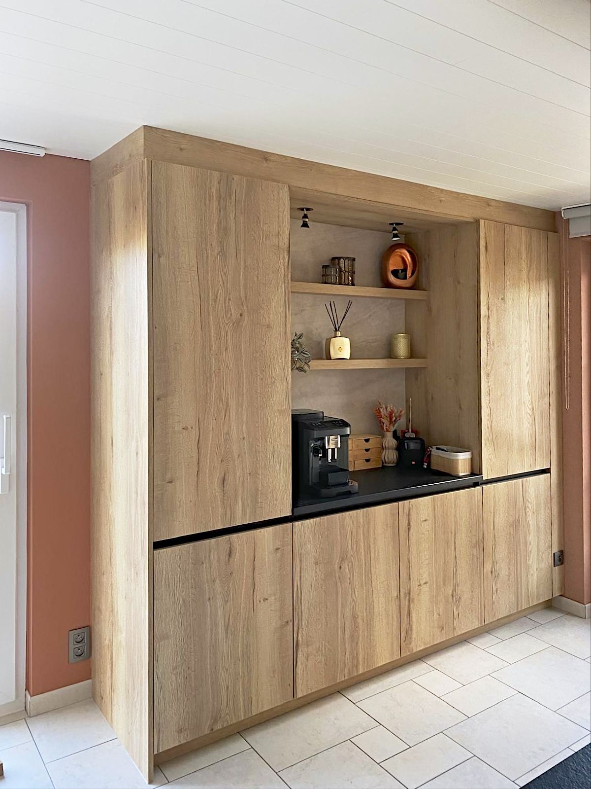 Hoge kastenwand in een houttint met een verlichte nis voor de koffiemachine