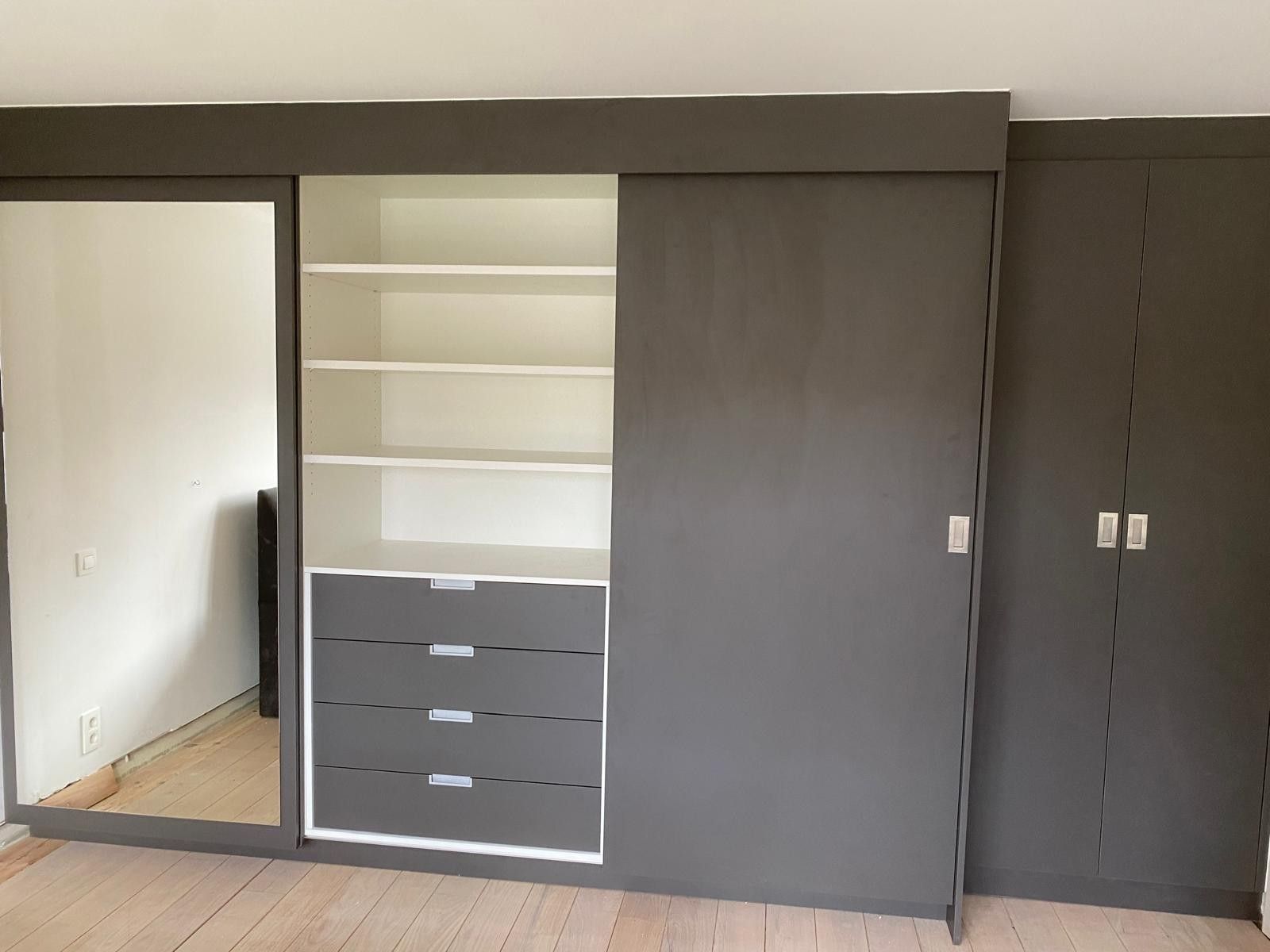 Kastenwand in antraciet met een spiegel, een open vak met planken en vier lades, een schuifdeur en een hoge kast met twee deuren
