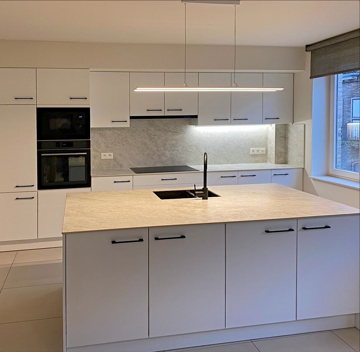 Witte keuken met zwarte grepen, een eiland met spoelbak en een achterwand in steenlook